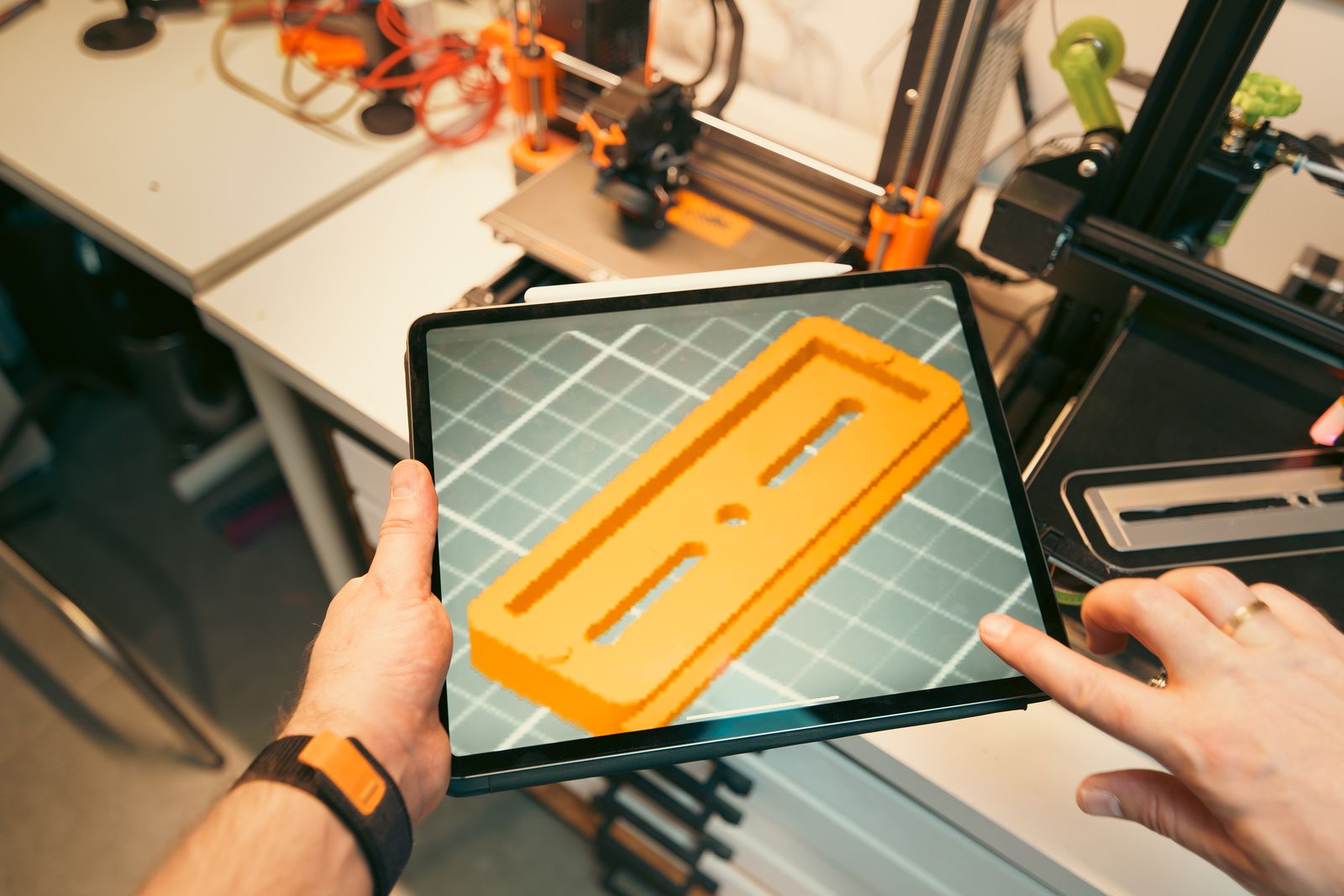 Engineer reviewing a 3D printed part on a tablet next to FDM printers in a workshop