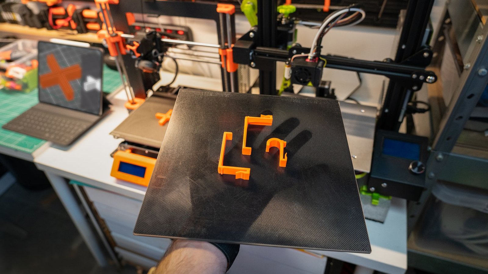 Batch of orange FDM parts on a build plate in a production workshop